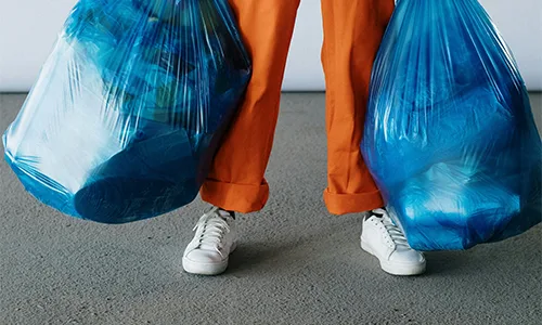 Man holding two blue big garbage bags