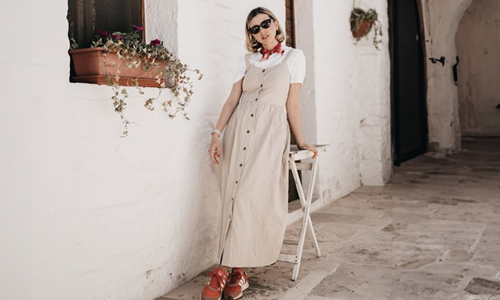 woman-in-beige-dress-standing-next-to-white-wall